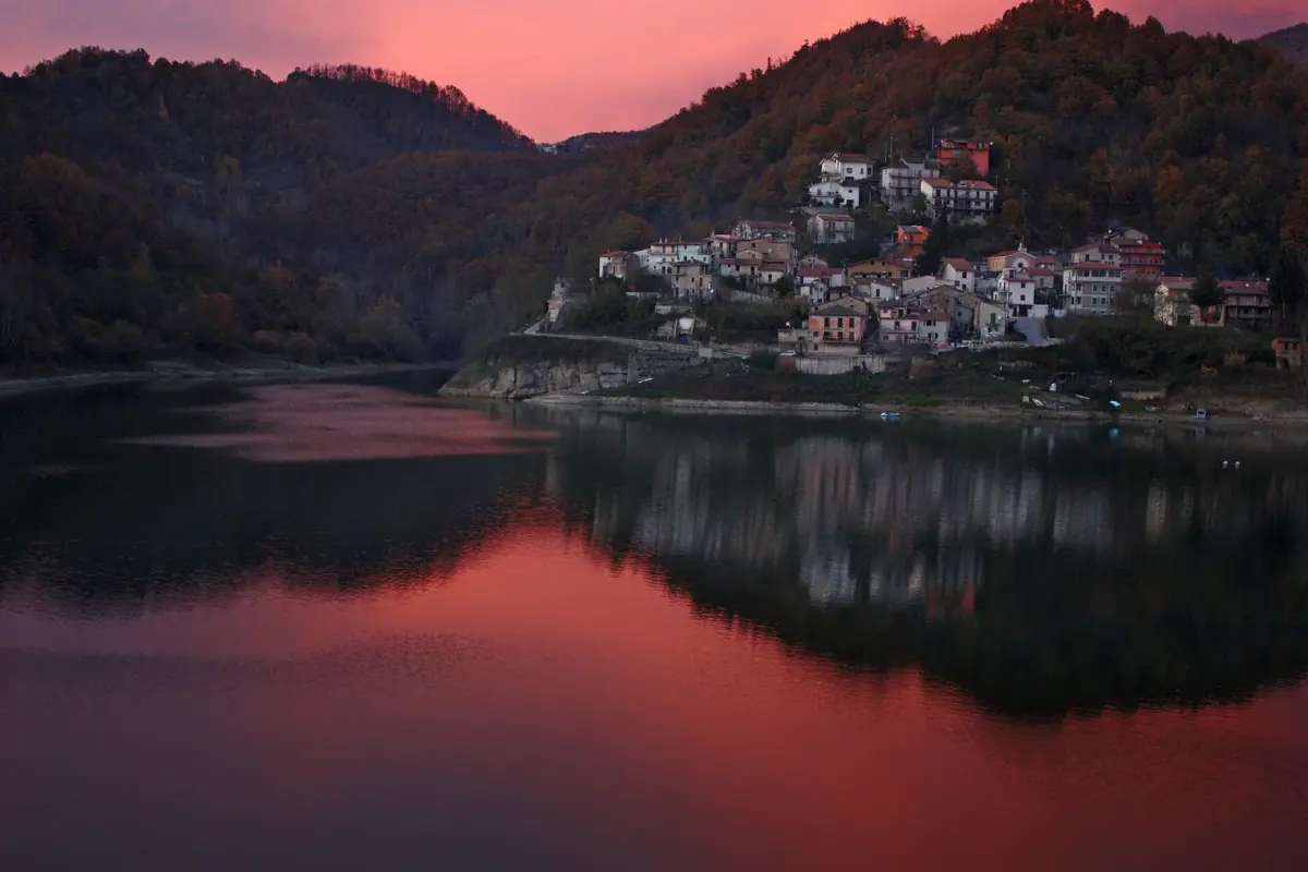 Il paese di Fiumata riflesso nel lago sotto un cielo rosso al tramonto