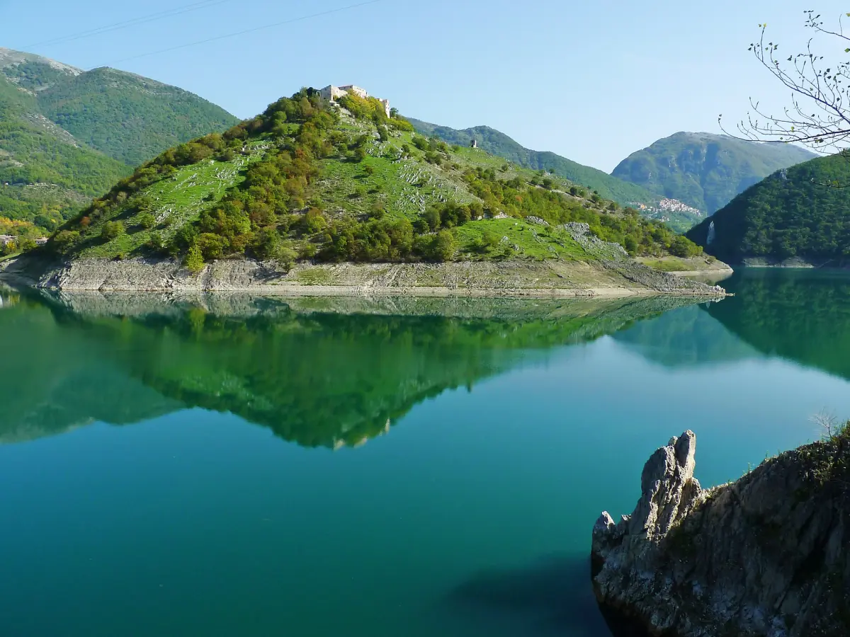 Colle verde con un castello in rovina riflesso nel Turano calmo