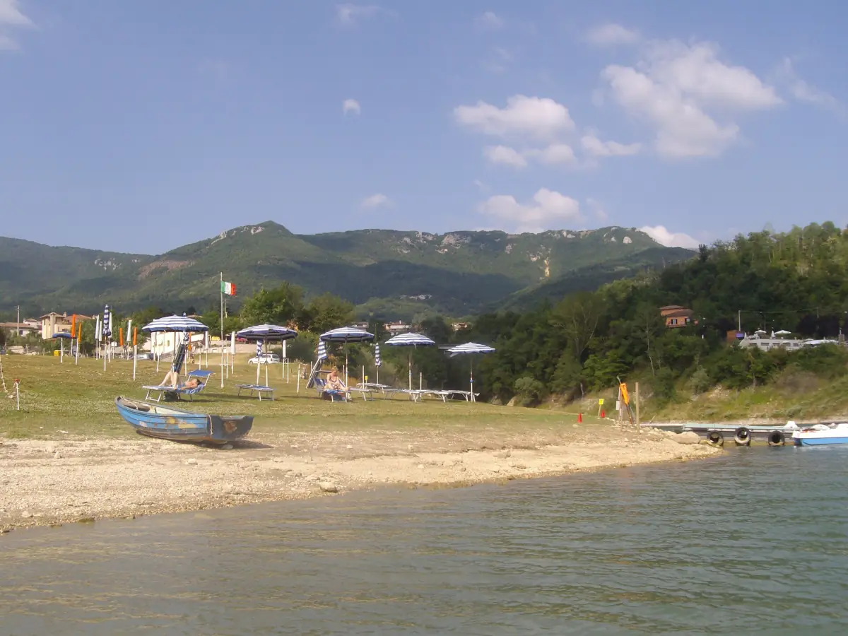 Spiaggia sabbiosa del lago a Miralago con ombrelloni e una barca